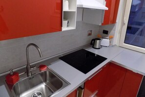 Una cocina moderna con pileta de acero inoxidable, cocina por inducción negra y muebles color rojo.
