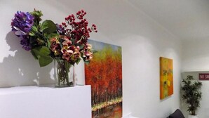 Een kamer met een witte plank, een vaas met bloemen en twee schilderijen aan de muur.