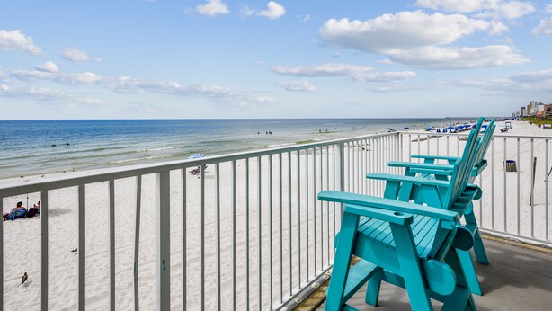 A beach view with turquoise chairs and a white railing.