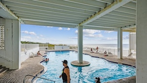 A swimming pool with a view of the ocean, surrounded by lounge chairs and a covered area.