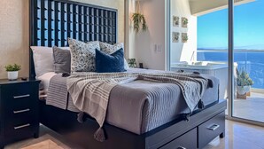 A modern bedroom with a large bed, a dark headboard, and a view of the ocean through a sliding glass door. - LuxuryCorner-PrivateJacuzzi-LasOlasCondo-Rosarito (Playas de Rosarito)