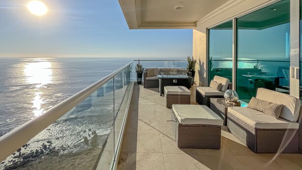 A balcony with a glass railing overlooking a body of water, furnished with sofas and a table. - LuxuryCorner-PrivateJacuzzi-LasOlasCondo-Rosarito (Playas de Rosarito)