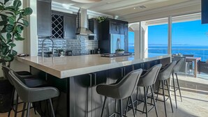 A modern kitchen with a large island, bar stools, and a view of the ocean. - LuxuryCorner-PrivateJacuzzi-LasOlasCondo-Rosarito (Playas de Rosarito)