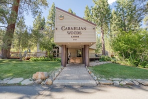 A lodge entrance with a sign reading 'CARNELIAN WOODS LODGE 5101,' surrounded by trees and a paved pathway.