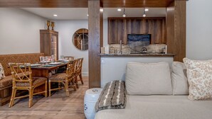 Un comedor con una mesa de madera dispuesta para cuatro personas, rodeada de sillas de mimbre. Un sofá con cojines estampados se encuentra frente a una chimenea de piedra.