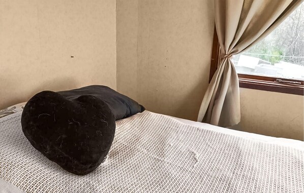 Un lit recouvert d’une couverture blanche à motifs, un oreiller foncé et une fenêtre avec des rideaux.