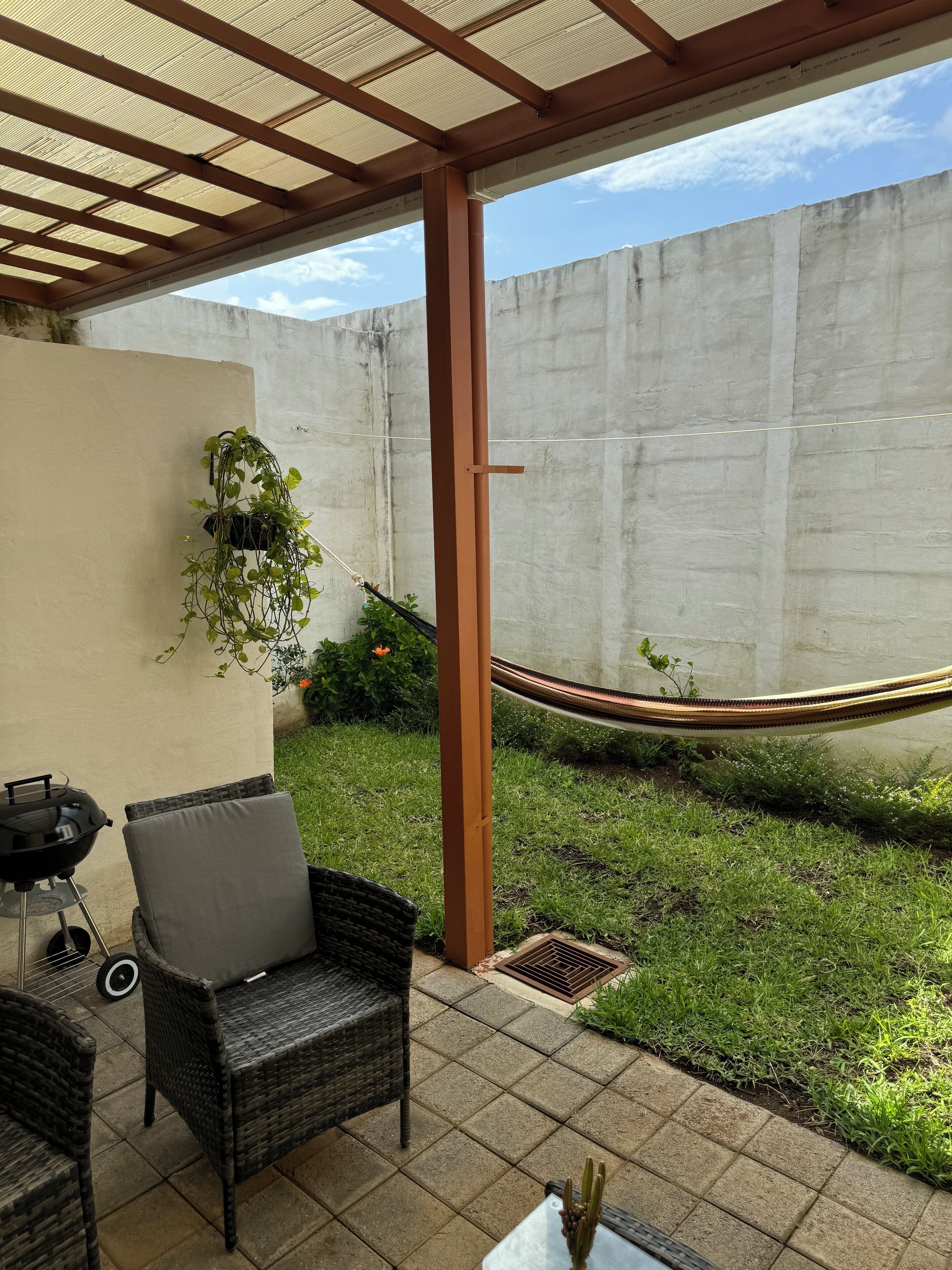 A patio area with a grill, wicker furniture, a hammock, and a concrete wall.