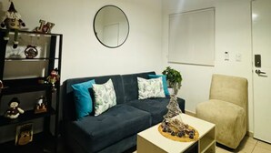 A living room with a dark blue sofa, a beige armchair, a coffee table with a decorative item, a round mirror on the wall, and a ceiling light. - Charming 2-bedroom house in Santa Ana with WiFi and AC (Santa Ana)