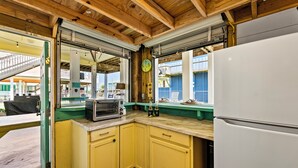 A kitchen with wooden beams, a refrigerator, a microwave, and a window overlooking a balcony. - Beach Retreat | Views, Bar, BBQ, Arcade, Games, Fenced Yard, Deck, Steps to Sand (Port Bolivar)