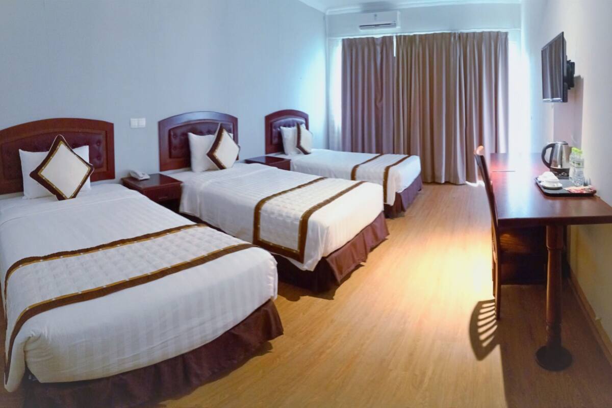 Une chambre d’hôtel avec trois lits, des têtes de lit en bois et un bureau équipé d’une machine à café.