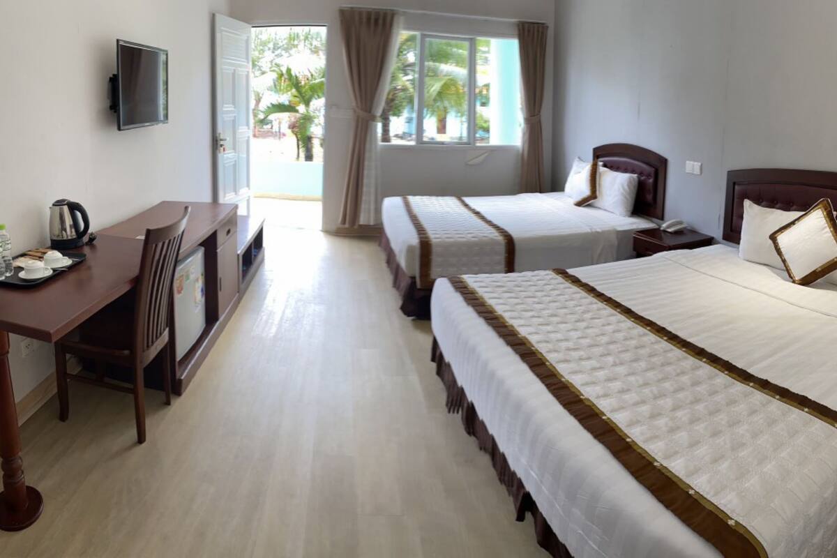 Une chambre d’hôtel avec deux lits, un bureau, une chaise, une télévision et une fenêtre avec des rideaux.