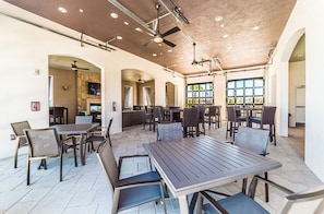 A spacious indoor dining area with multiple tables and chairs, ceiling fans, and a large window providing natural light.