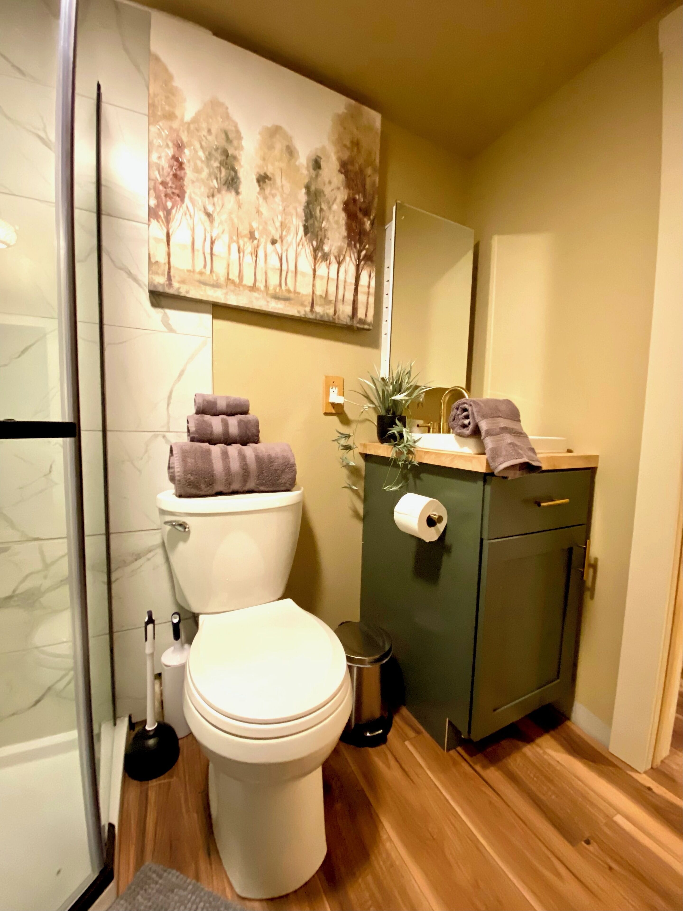 A compact bathroom with a toilet, a sink, a mirror, and a painting above the sink.