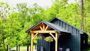 A rustic wooden cabin with a porch, two chairs, and hanging flower baskets. - Charming Cottage Retreat in Lewistown – Sleeps 4 (Lewistown)