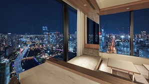 Ein modernes Hotelzimmer mit großen Fenstern und Blick auf die beleuchtete Stadt bei Nacht.