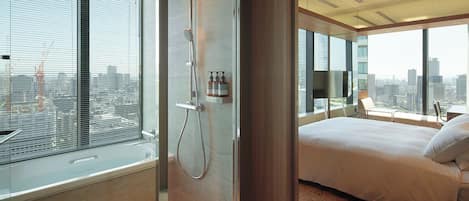 Un dormitorio moderno con una cama grande, cabina de ducha de vidrio y vistas a la ciudad.