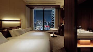 A hotel room with a large bed, a desk, and a view of a cityscape at night.