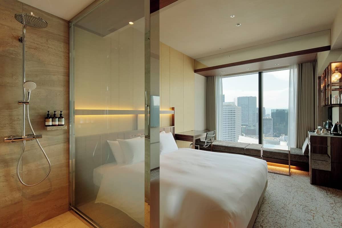 Une chambre d’hôtel moderne dotée d’une douche en verre, d’un lit, d’un bureau et offrant une vue sur la ville.