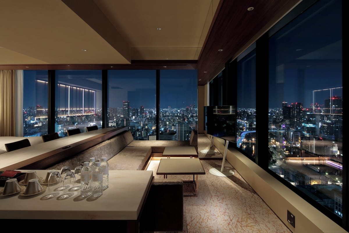 Une chambre d’hôtel moderne avec vue sur la ville, un canapé, une table à manger avec des verres et un téléviseur.