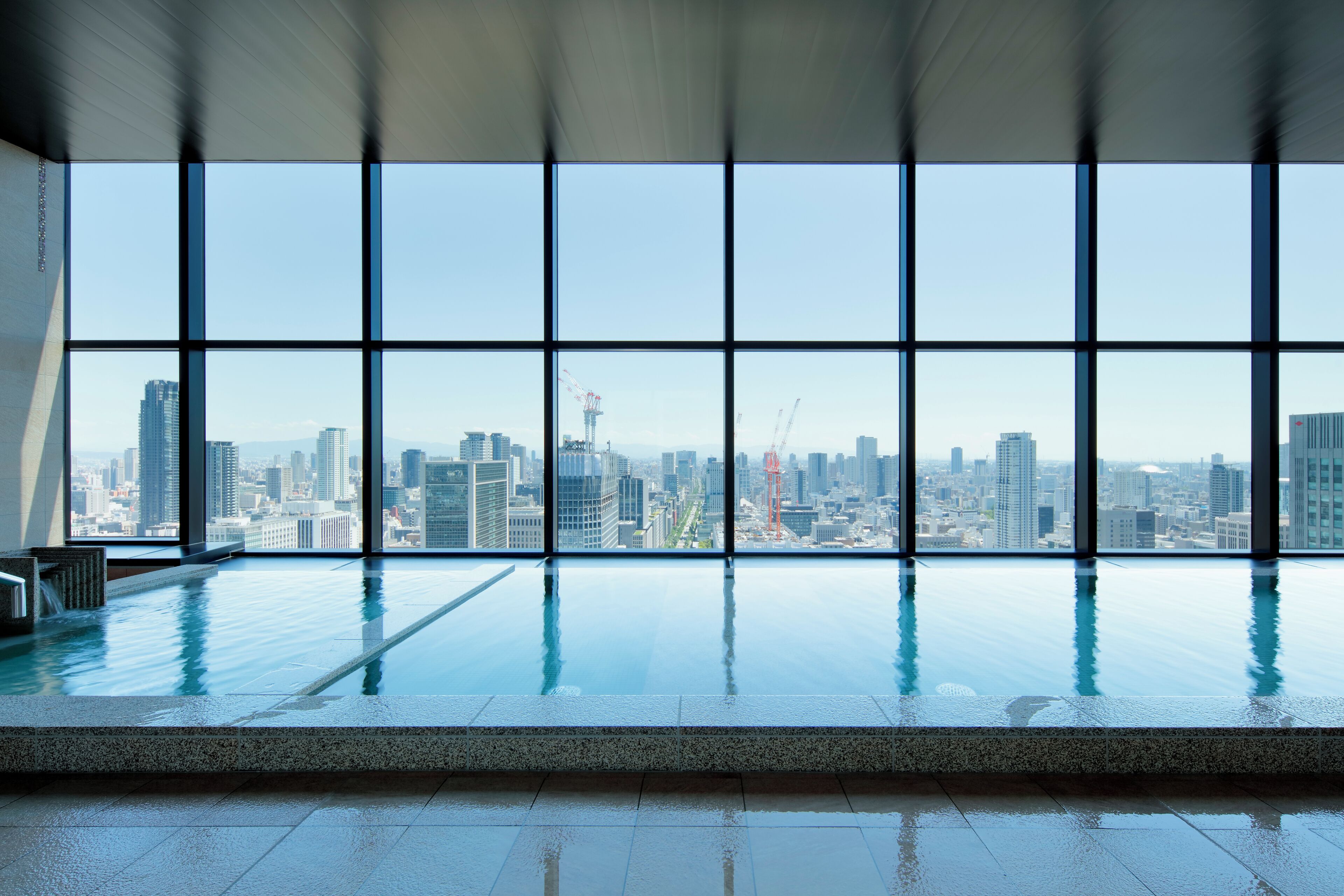 Piscina interior moderna con vistas a la ciudad a través de amplios ventanales.