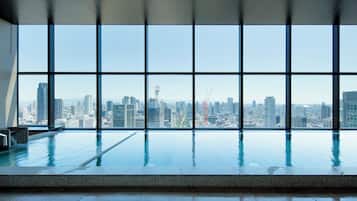 Piscina interior moderna con vistas a la ciudad a través de amplios ventanales.