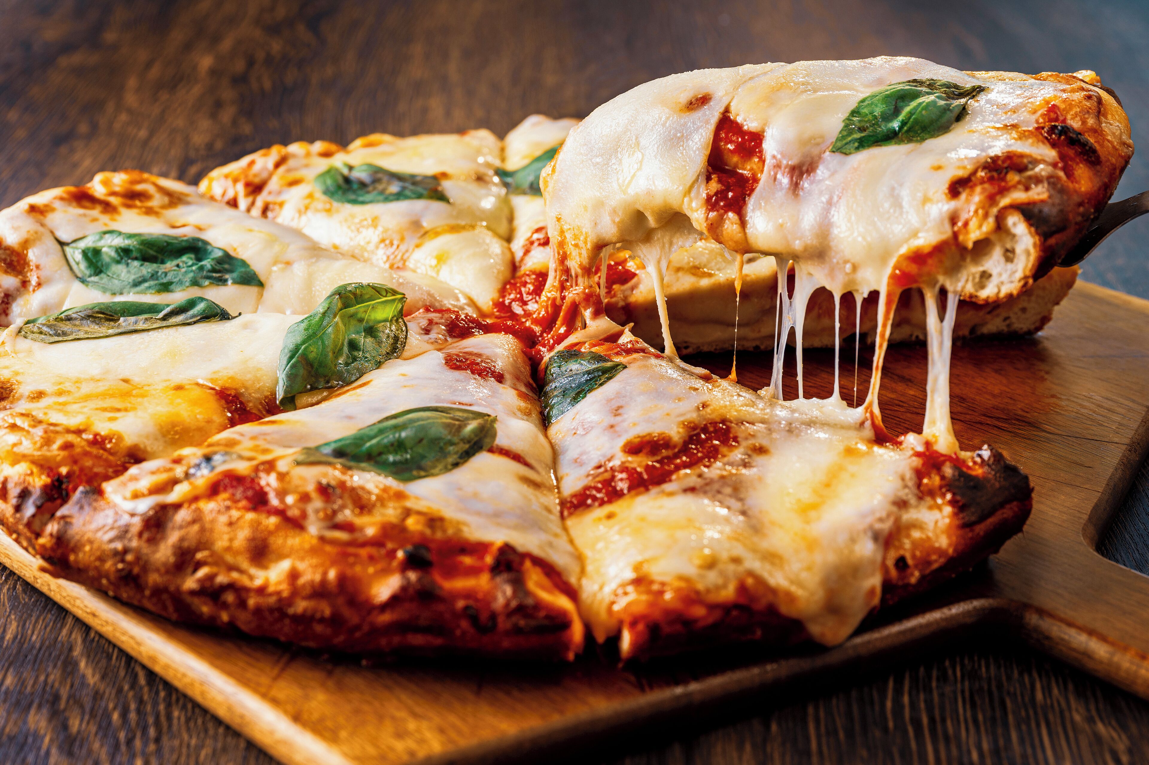 A pizza with cheese and basil leaves on a wooden board.