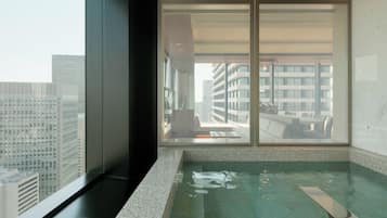 A modern room with a large window, a built-in hot tub, and a view of city buildings.