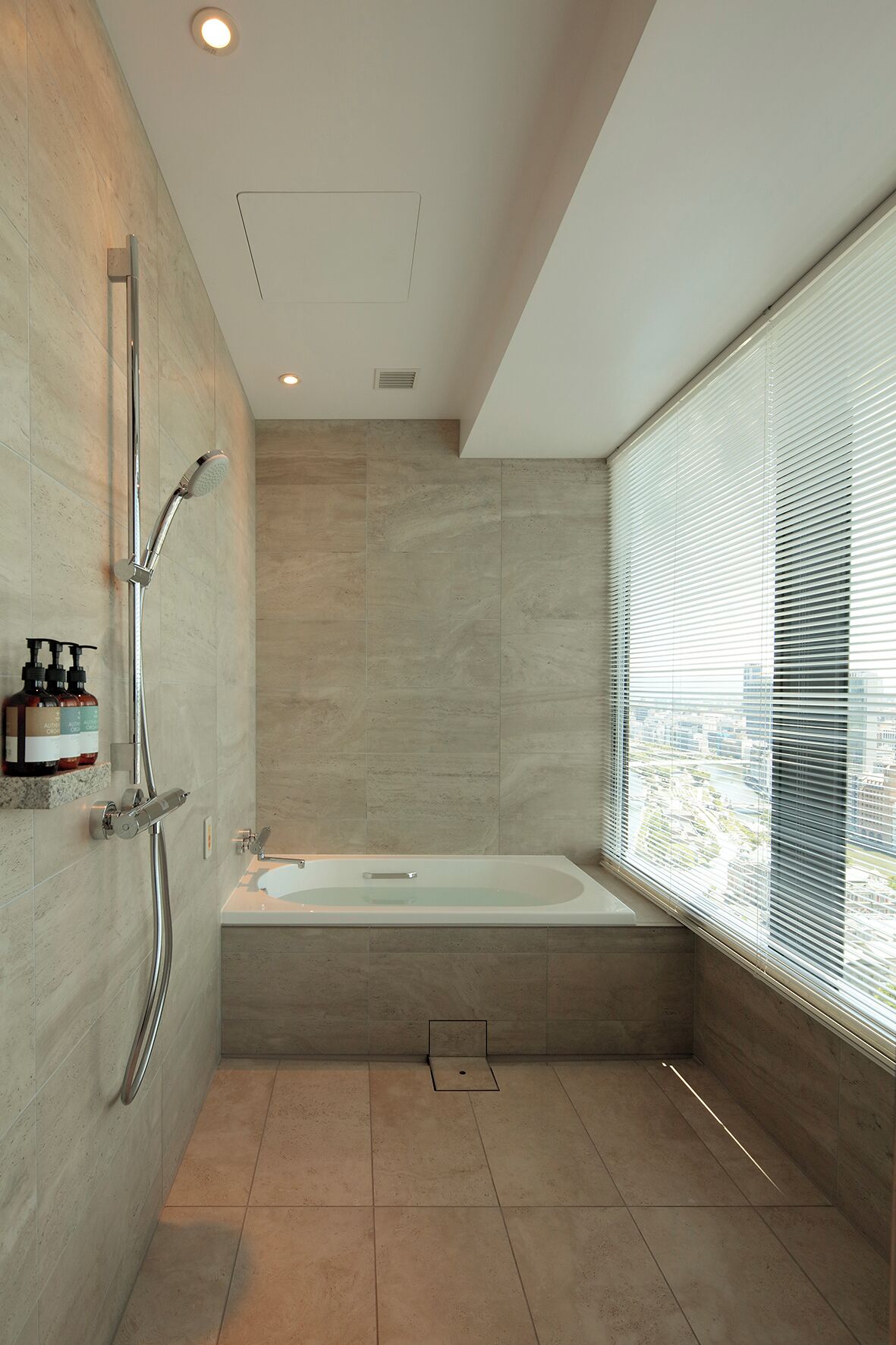 A modern bathroom with a bathtub, a shower, and a window with blinds.