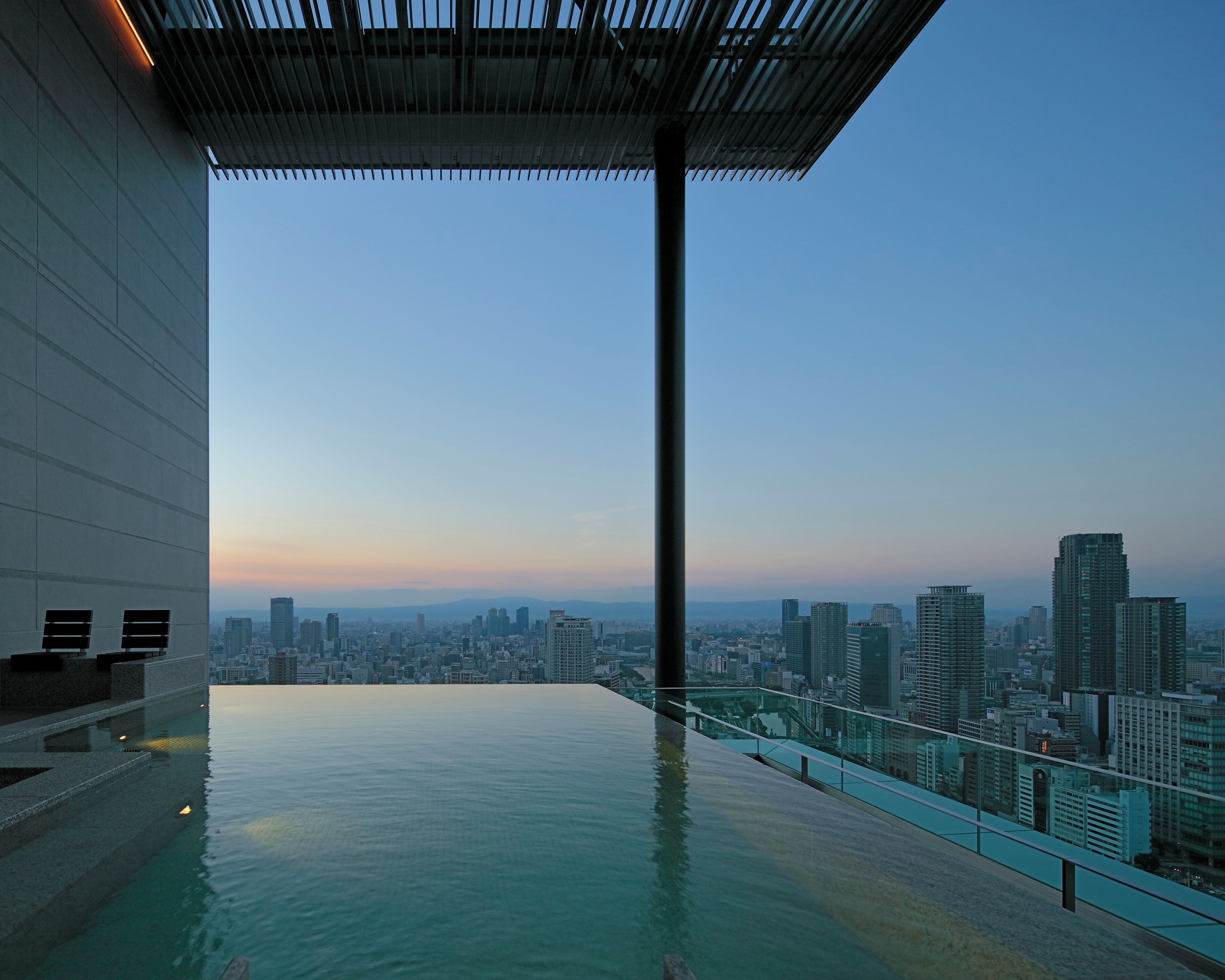A rooftop infinity pool with a cityscape view, a glass railing, and a modern architectural design.