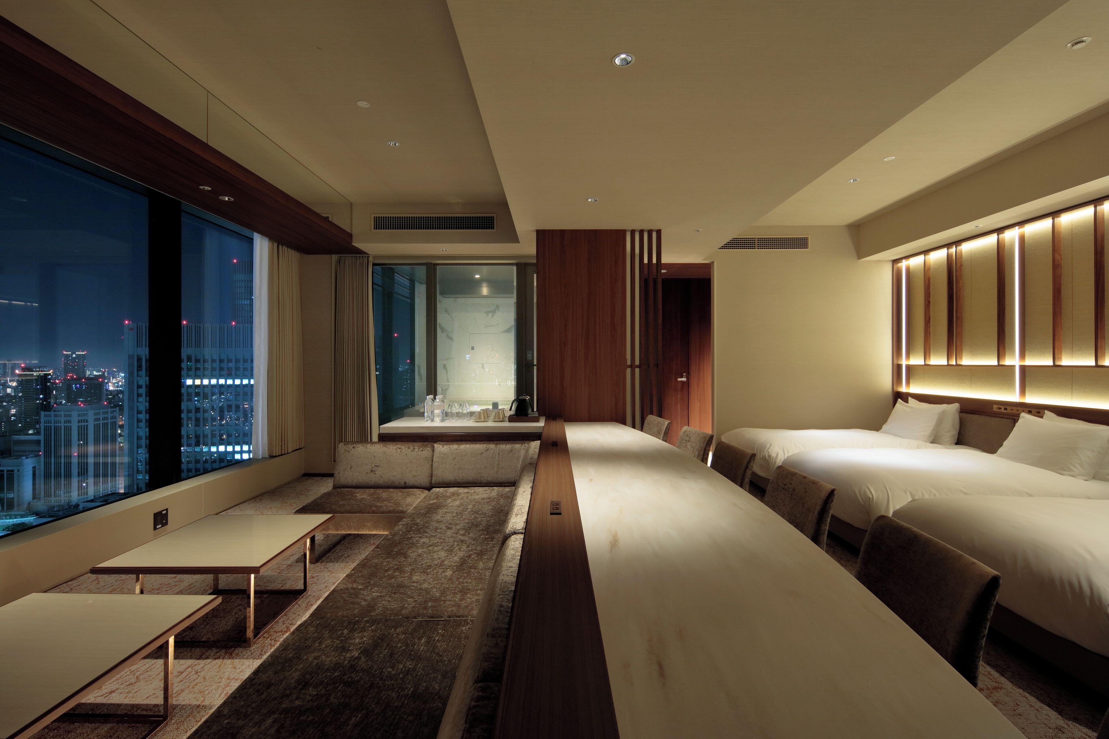 A modern hotel room with a large bed, a seating area, and a view of the city at night.