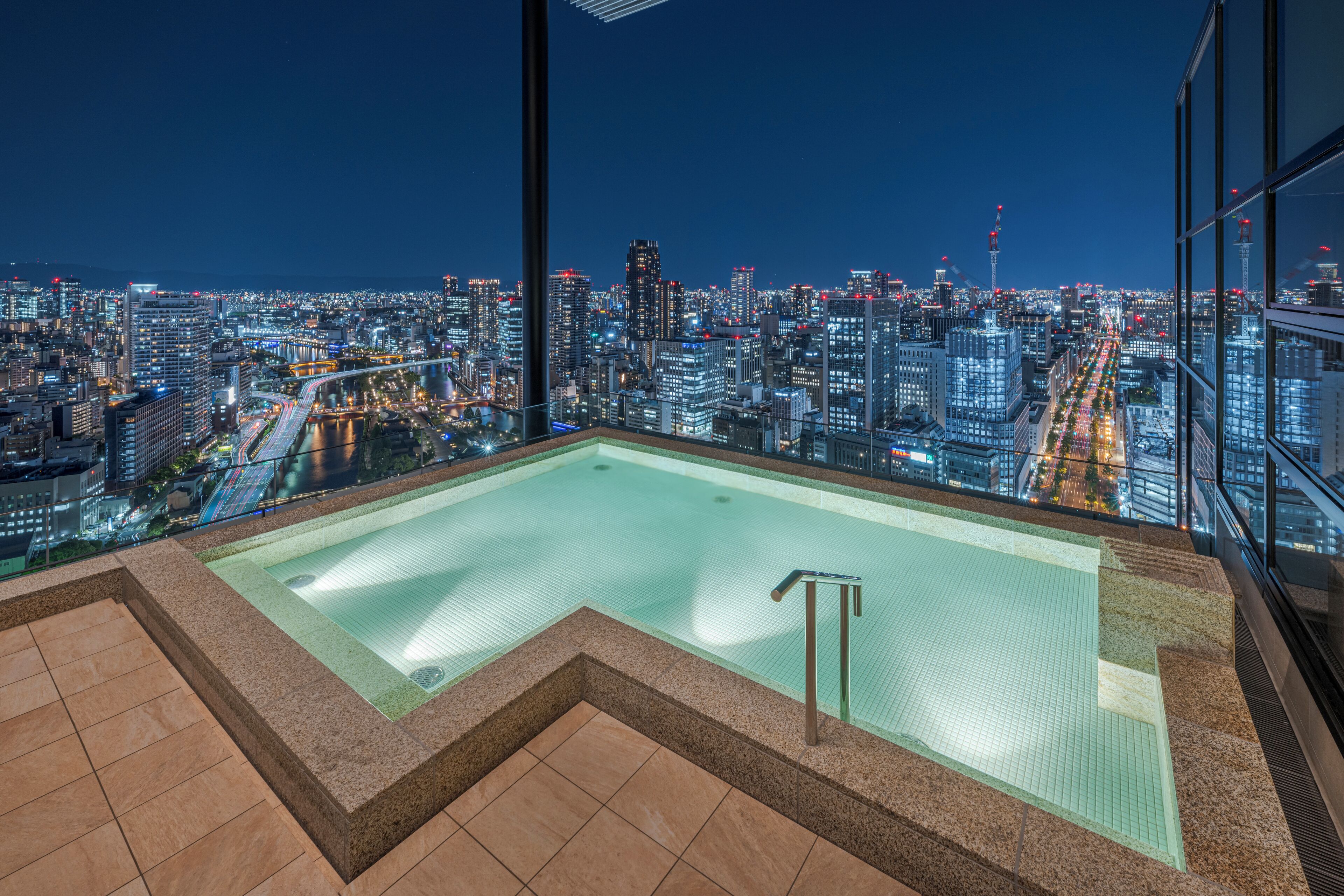 A rooftop pool with a cityscape view, surrounded by glass railings.