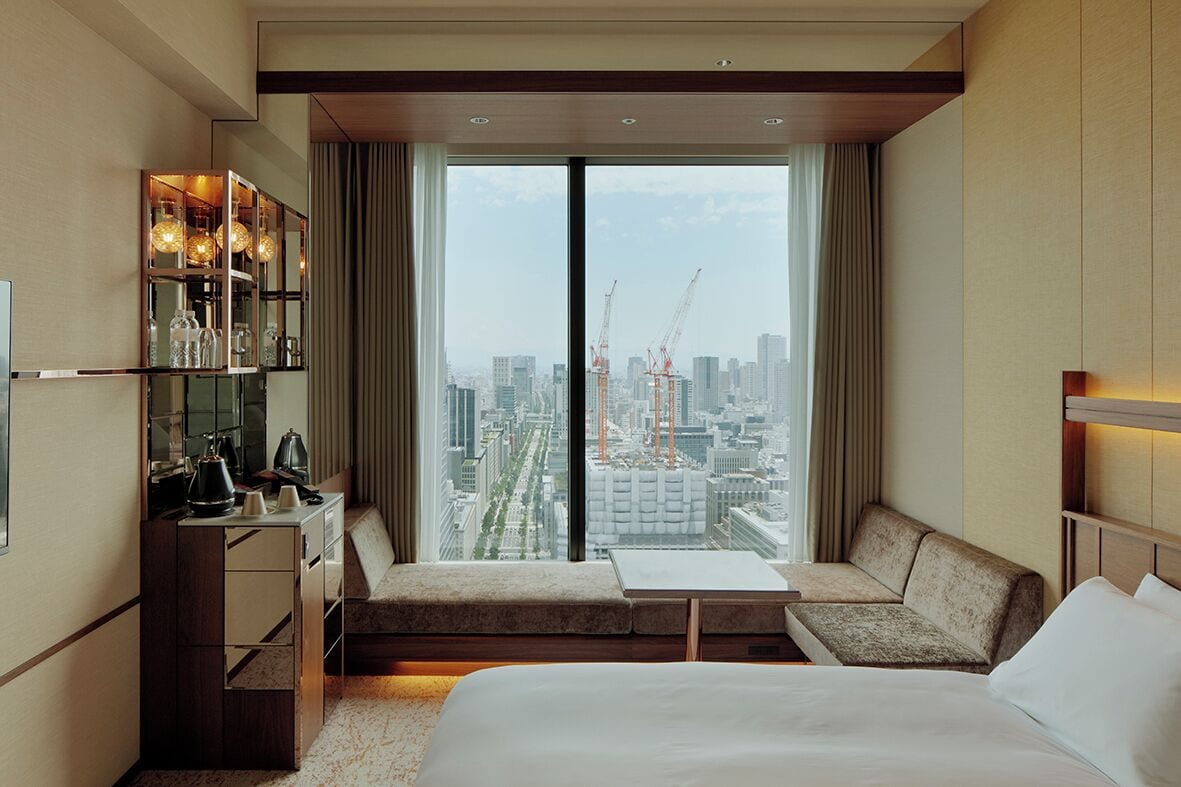 A hotel room with a large bed, a seating area with a view of the city, and a minibar.