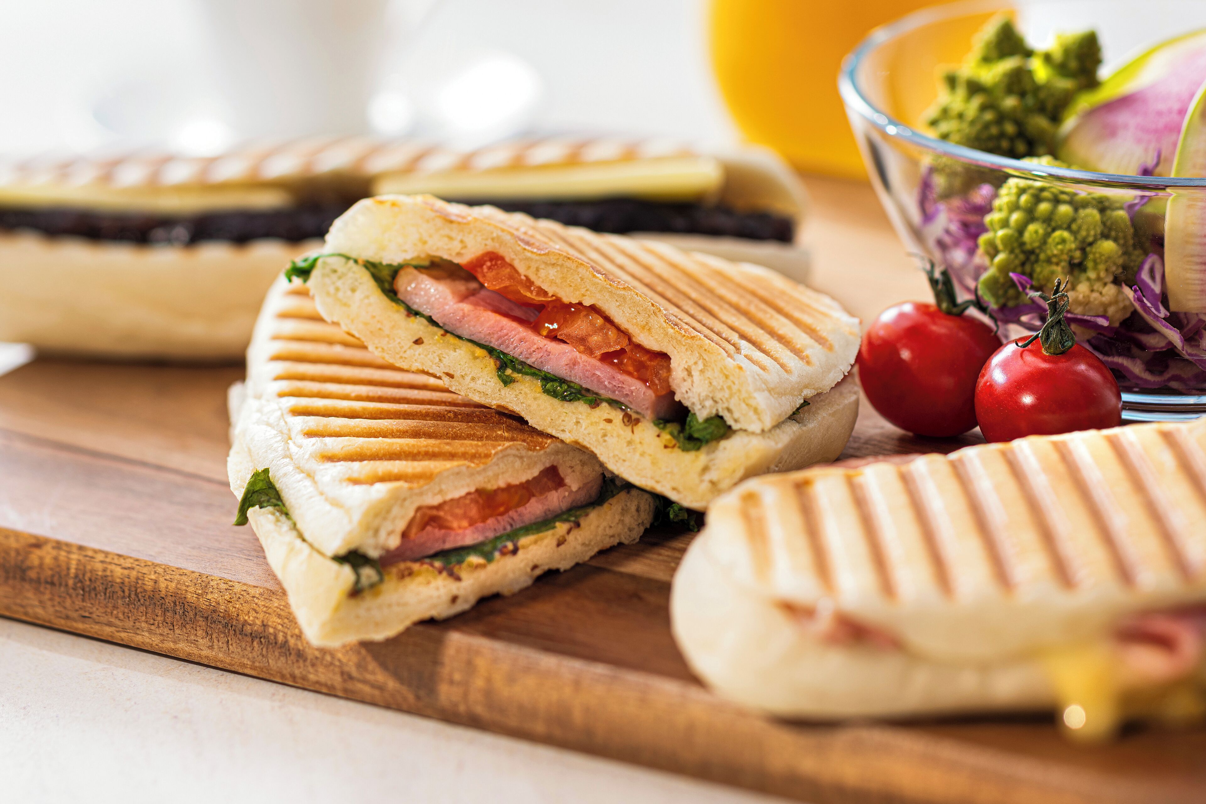 A sandwich cut in half with visible ingredients like lettuce, tomato, and ham, placed on a wooden board.