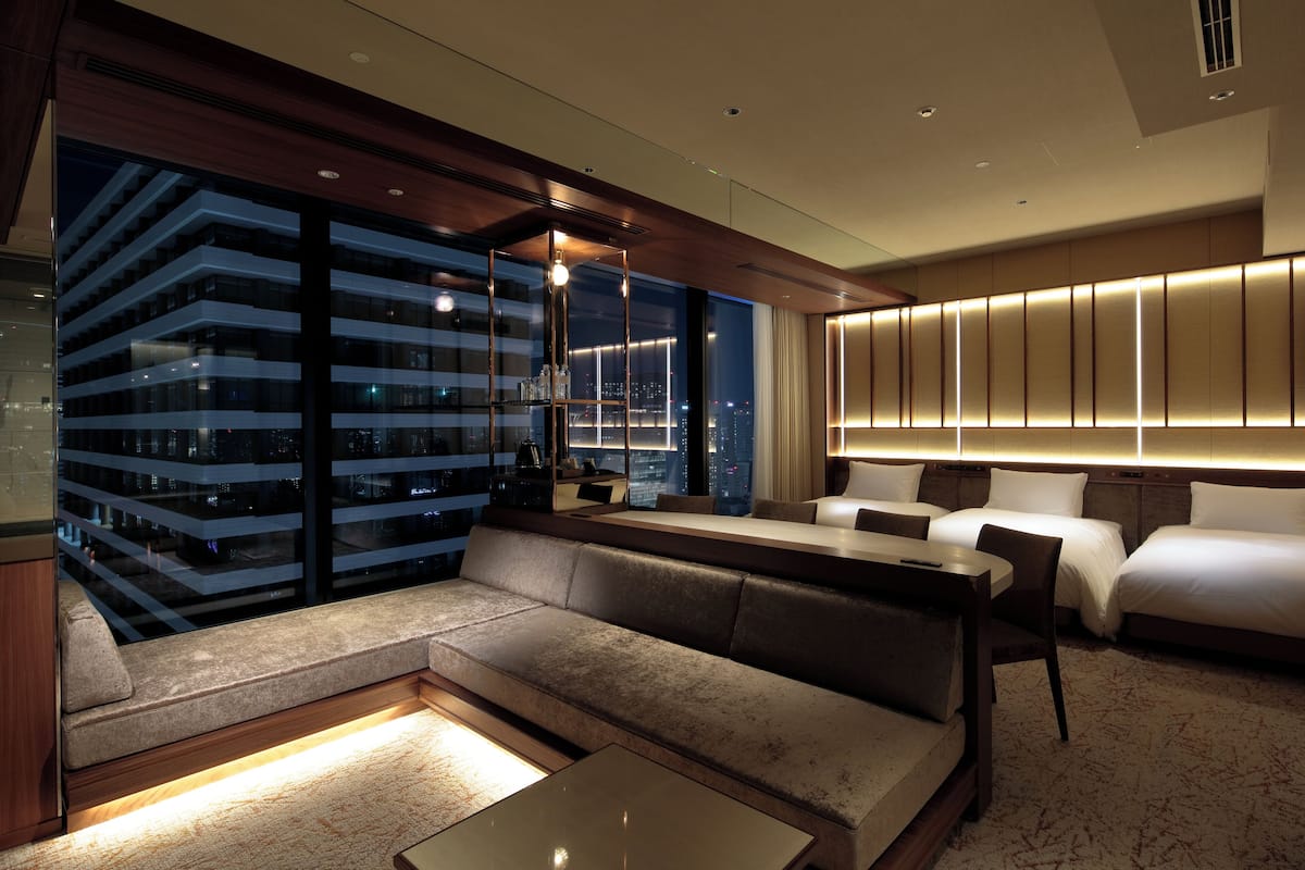 Une chambre d’hôtel moderne dotée d’une grande fenêtre, d’un canapé, d’une table à manger et d’un mini-bar.