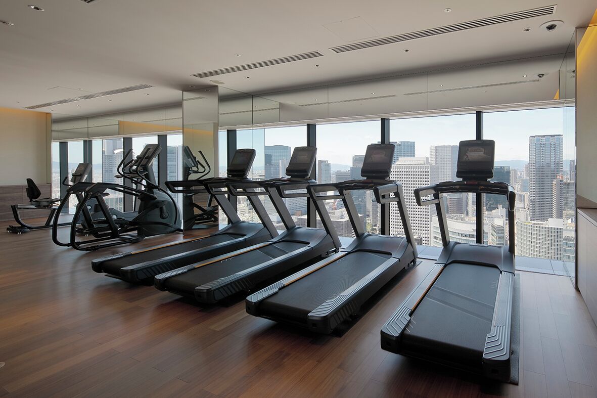 A modern gym with treadmills, exercise bikes, and a large window offering a city view.