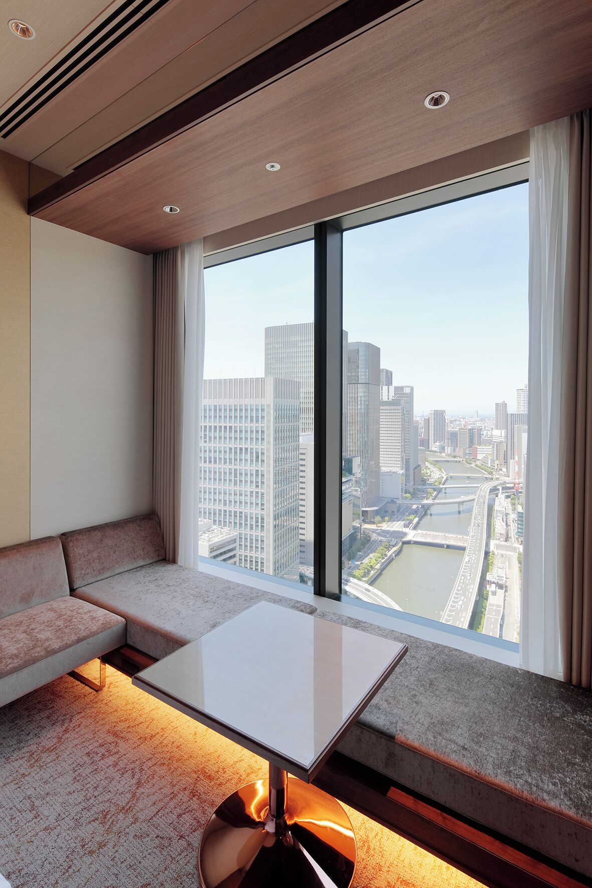 Une chambre d’hôtel moderne dotée d’une grande fenêtre donnant sur la ville, d’un canapé et d’une petite table.