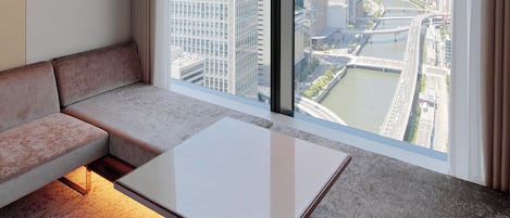 Habitación de hotel moderna con un ventanal amplio que ofrece vistas a la ciudad, un sofá y una mesita.