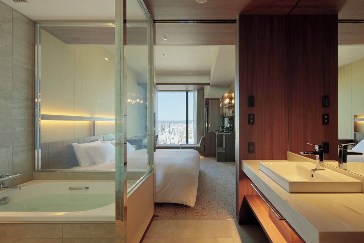 Une chambre d’hôtel moderne dotée d’un grand lit, d’une salle de bain séparée avec baignoire et offrant une vue sur la ville.