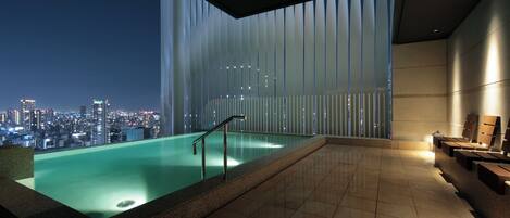 A modern indoor pool with a cityscape view, a glass wall, and a seating area.