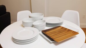 Una mesa redonda para comer con platos y tazones blancos apilados, y una sola bandeja de madera.