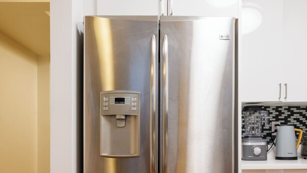 Un refrigerador de acero inoxidable con dispensador de agua, en una cocina con armarios blancos y piso de madera.