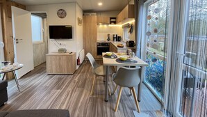 Cocina compacta con comedor, televisor montado en la pared y ventana con cortinas.