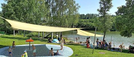 En park med en vattenlekplats, ett avskärmat sittområde och en sjö.