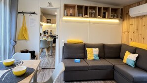 Una sala de estar moderna con un sofá modular, una mesa de comedor con individuales amarillos, y un área de cocina visible a través de un umbral abierto.