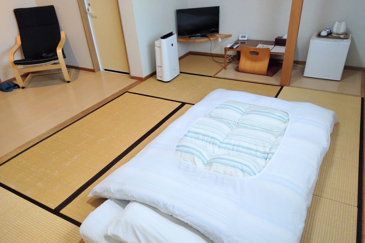 Una cama bien hecha con un cojín a rayas y un suelo de esteras de tatami.