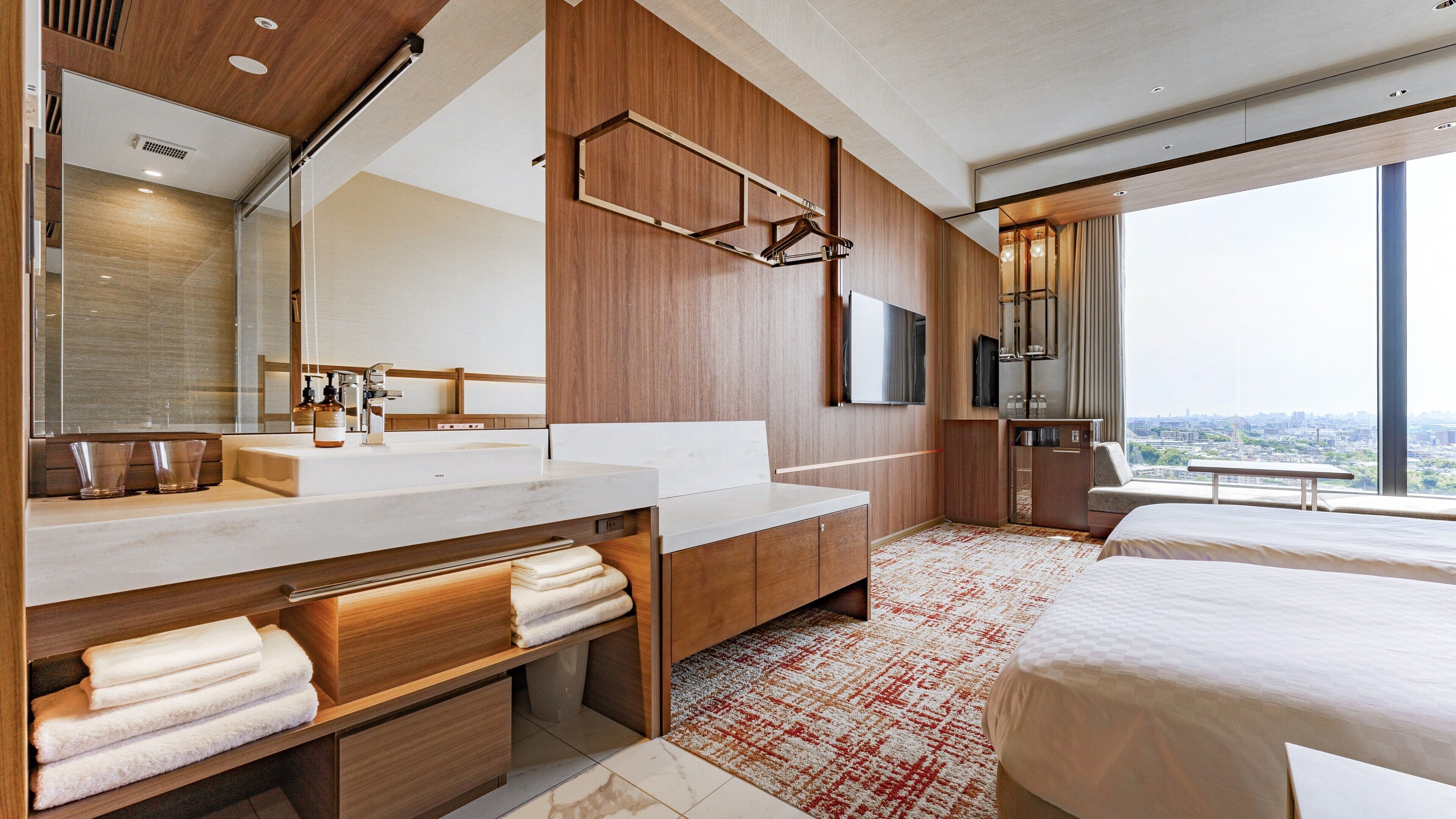 Ein modernes Hotelzimmer mit einem großen Bett, einem Badezimmer mit großem Spiegel und Waschbecken sowie Blick auf die Stadt.