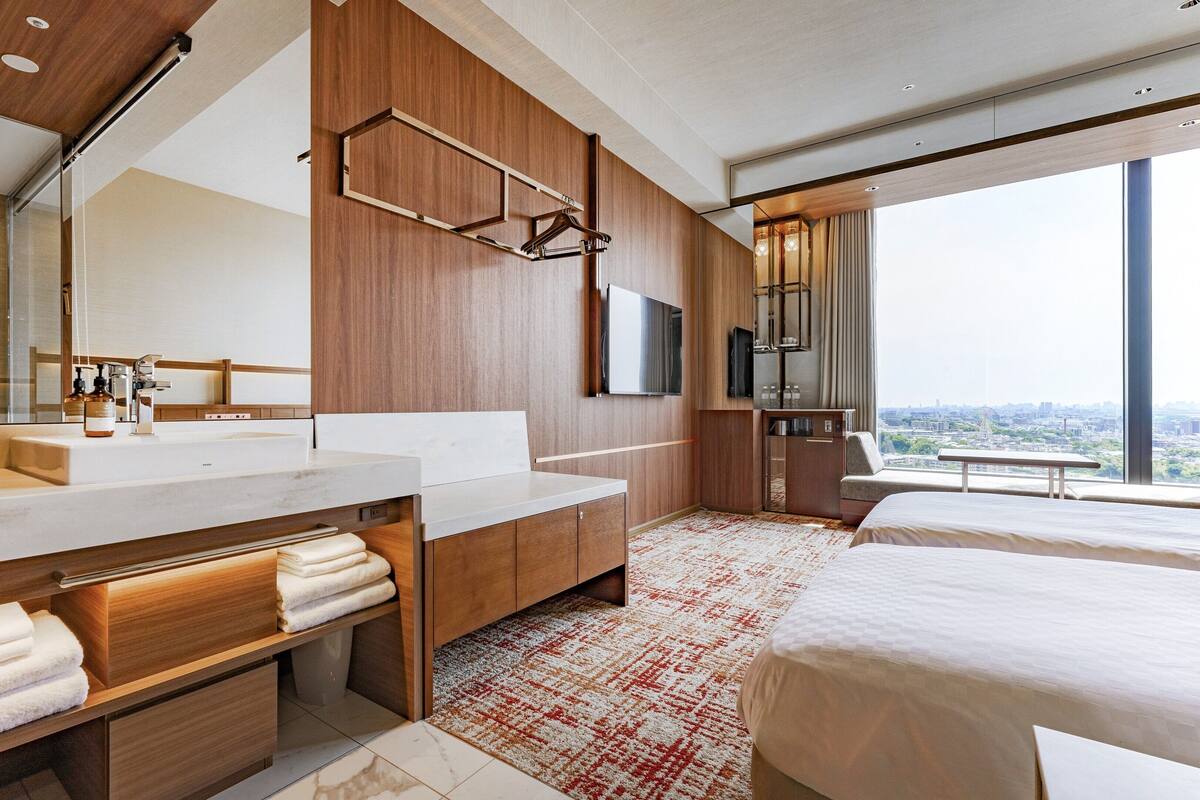 Een moderne hotelkamer met een groot bed, een badkamer met een grote spiegel en wastafel, en uitzicht op de stad.