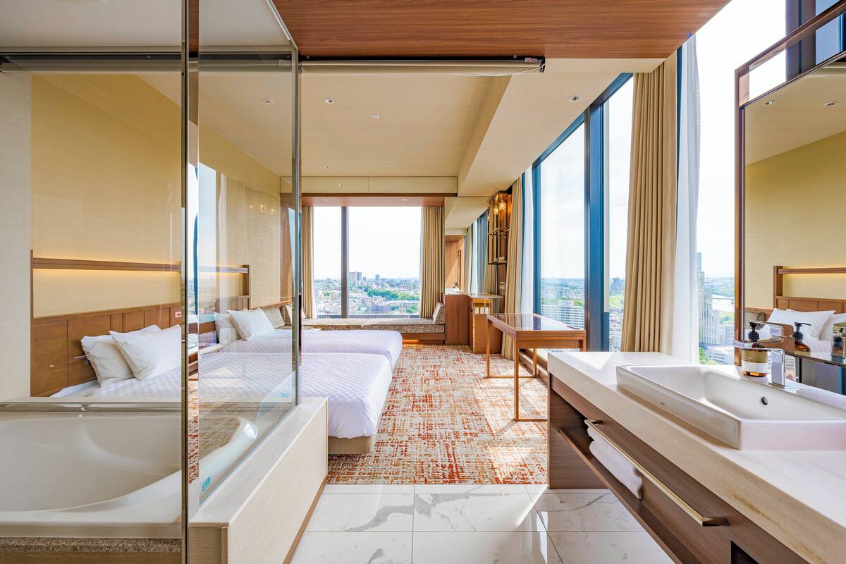 Een moderne hotelkamer met een groot bed, een bureau, een badkamer met een grote spiegel en uitzicht op de stad.
