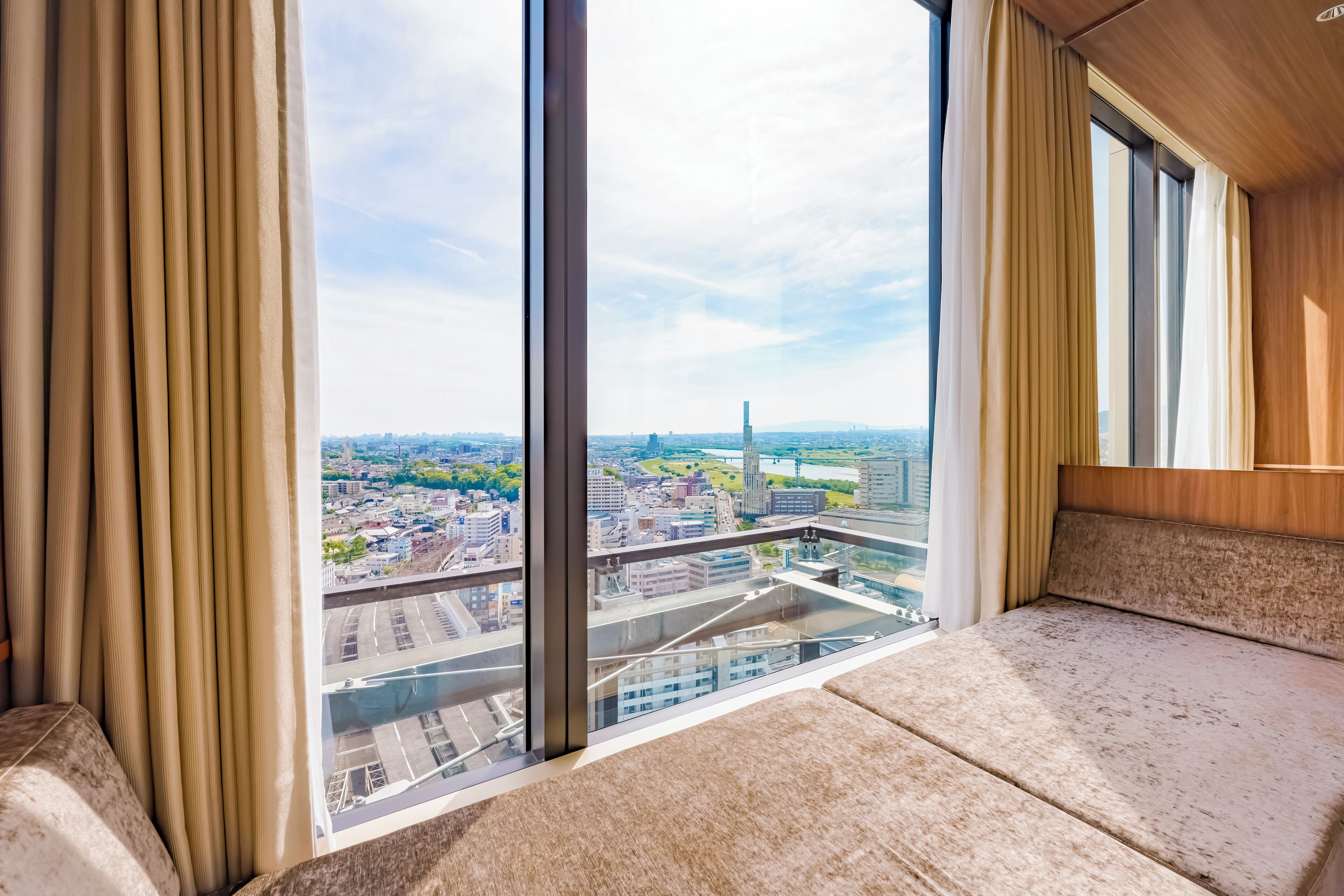 Habitación en un rascacielos con un ventanal grande que ofrece vistas de la ciudad, un banco acolchado y un techo de madera.