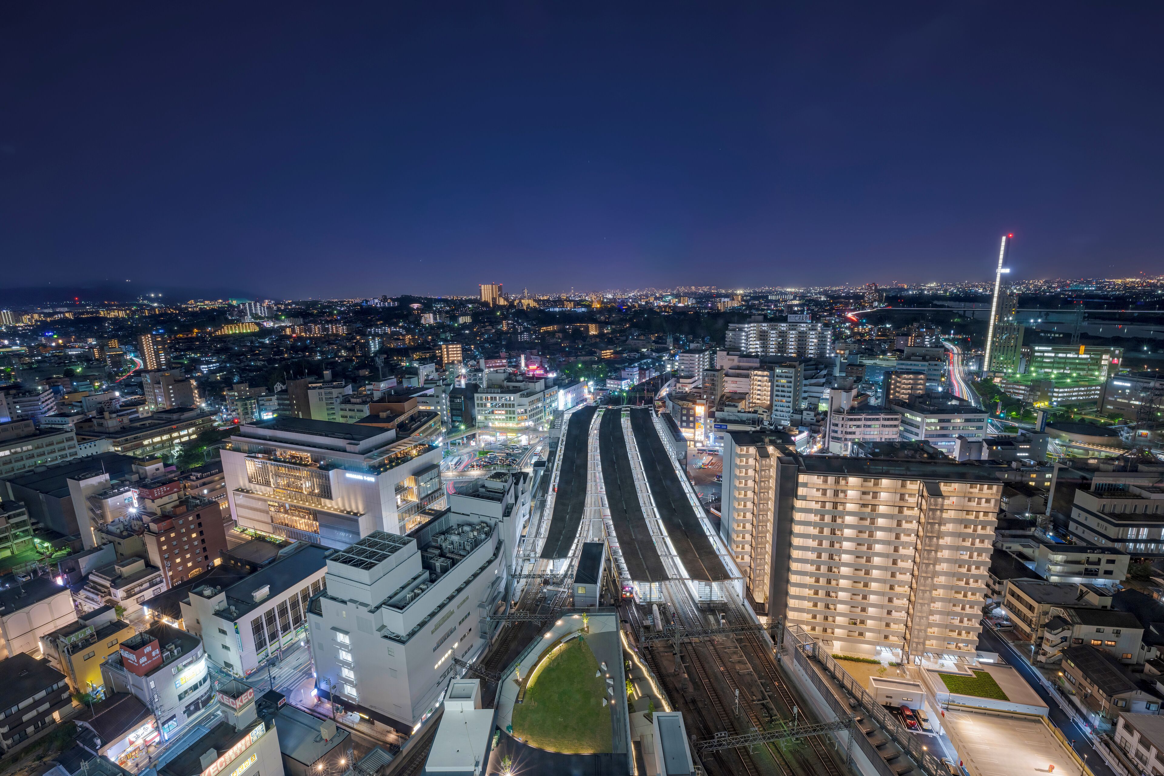 A nighttime cityscape with a prominent train station and surrounding buildings.